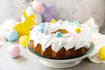 Glazed easter lemon cake decorated with confectionery and mini chocolate eggs candy on gray stone background. Happy Easter holidays, tasty dessert. Copy space.