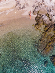 top down view of a girl in a bikini lying on the sand on the seashore; relaxing on a paradise beach as seen from a drone; a beautiful model lying on the sand