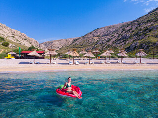 beautiful girl in bikini swims on a strawberry-shaped mattress in turquoise water in oprna bay on...
