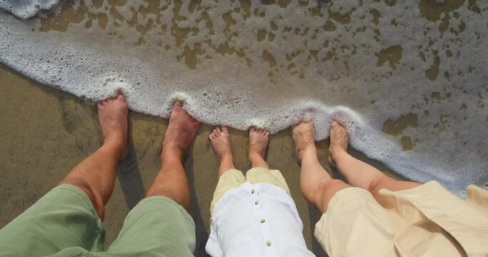 Tanned bare feet of three people on golden sandy beach, pov. Last day of summer vacation, which three family members spend on beach. The family spends their last day off on beach, urine feet in sea