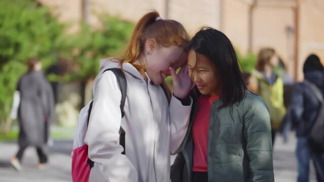 Portrait of smiling cute teen girl listening gossips as classmate whispering on ear. Realtime