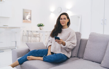 Smiling woman with smartphone sitting on sofa