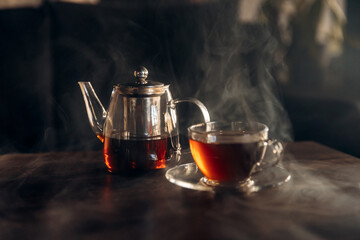 Close-up photo of a transparent teapot filled with tea and a transparent glass cup standing on a...