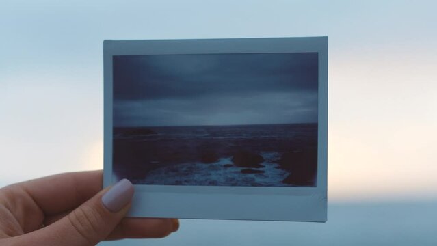 Hands, nature and photograph of a sea in the hand of a woman on the beach by the ocean at sunset with a view of the horizon and sky in the background. Travel, earth and polaroid with a female outside