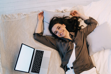 Happy woman resting on bed with netbook