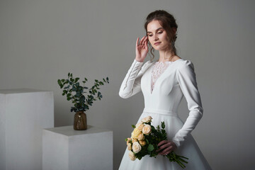 A beautiful young bride model in long lace dress in minimalist white studio interior. Wedding photography.