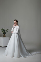 Fototapeta na wymiar A beautiful young bride model in long lace dress in minimalist white studio interior. Wedding photography.