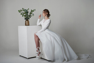 A beautiful young bride model in long lace dress in minimalist white studio interior. Wedding photography.