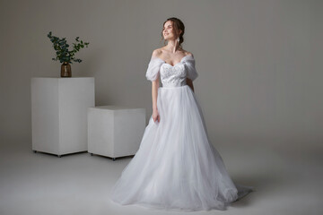 A beautiful young bride model in long lace dress in minimalist white studio interior. Wedding photography.