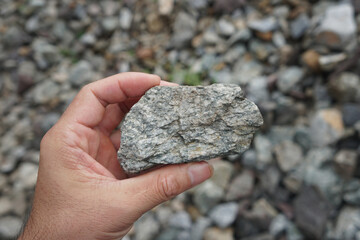 Sample raw specimen of granite igneous rock stone on Geologist's hand. The paving stones are used...