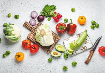 Fresh various vegetables with wooden cutting boards and knife on white kitchen table top view. Cooking vegetarian meal from healthy ingredients, diet food and nutrition concept