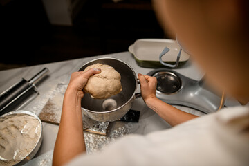 view on female hands holding bread dough over stainless bowl on table