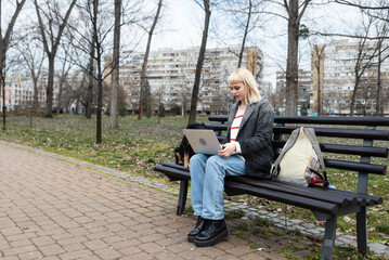 Fototapeta premium Young university girl sitting on bench with adopted dog working on laptop. She left the apartment for her student roommate boyfriend they need privacy because they share rented apartment or room