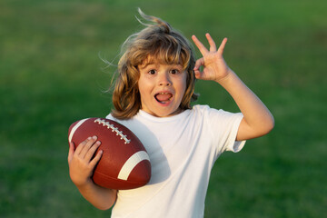 Kids and sports. Young boy playing american football. Kid boy playing with rugby ball in park. Child holding rugby ball while playing american football in Summer park. - obrazy, fototapety, plakaty