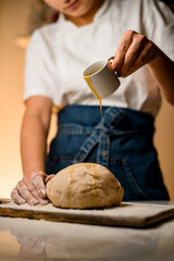 dough on cutting board with flour and female hand accurate pours oil from a cup onto it.