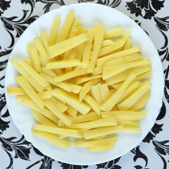 Raw french fries. Raw potatoes cut into strips, prepared for french fries, isolated on a white plate. Peeled potatoes. Cooking, raw vegetables