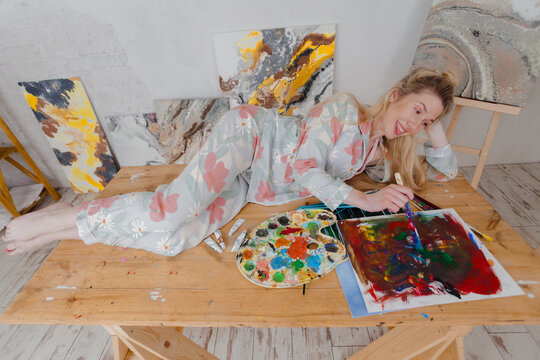 Talented happy Female Artist lying on the table and creating. Colorful, Emotional, Sensual Painter Creating Abstract Modern Art. Creative Expression concept.