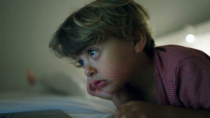 Child watching cartoons laying in bed hypnotized by screen at night
