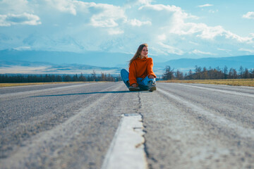 Happy traveling woman sitting on perfect asphalt road in mountains