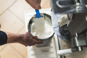 Close shot of man hands with a stirring paddle mixing ice cream from freezer in a steel container....