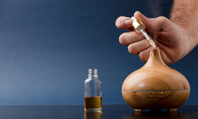 wooden air freshener with steam of natural essences, man's hand with dispenser refilling it, blue...