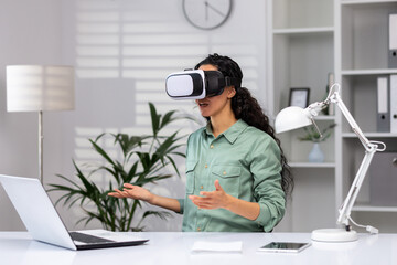 Obraz premium Successful latin american woman in office using vr glasses for video call and chatting online in virtual reality simulator, online conference with colleagues remote in metaverse.