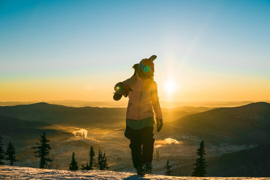 Silhouette of Skier female holding ski walking on mountain top during sunset above clouds, beautiful winter mountains landscape
