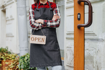 happy woman with sign open in her hands at restaurant or bar. working hours of coffee shop. wooden...