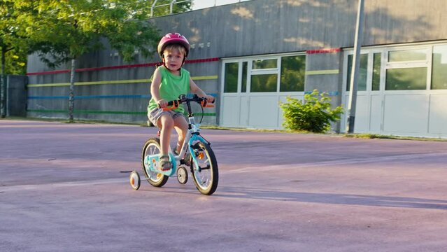 Small boy learn to ride bicycle with learning wheels, low angle