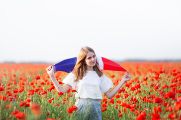 Beautiful girl holding waving flag of France in poppy field. National holidays concept: Armistice...