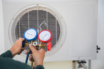 Air conditioning, HVAC service technician using gauges to check refrigerant and add refrigerant.