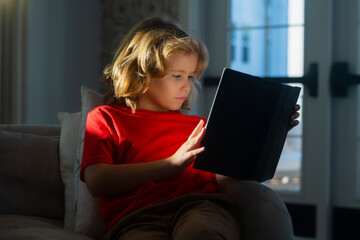 Elementary school nerd boy pupil read book. Kids and literature. Child reading book, sitting at home in cozy living room on couch.