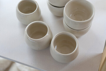 Obraz na płótnie Canvas creamy white background with ceramic pots and cups, shallow depth of field with focus on the first cups