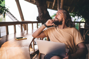 Pensive hipster guy with laptop technology thinking about remote working using 4g wireless internet...