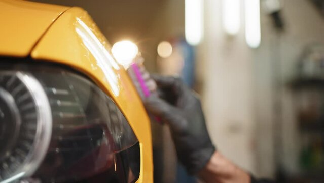 Applying nanoceramics to cars. Car paint protection concepts Professional male auto service worker polishing and detailing a car body, waxing car hood and headlight with a wax or nano ceramic coating