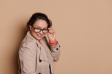Multi-ethnic mature woman in casual coat, smiling and looking at camera through stylish eyeglasses,...