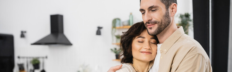 Fototapeta premium Bearded man hugging smiling wife at home, banner.