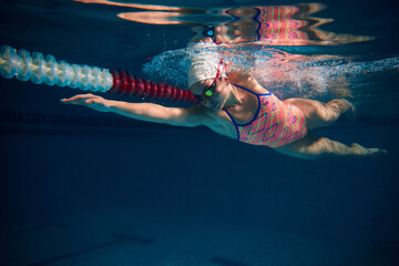Coordination of movements. Professional female swimmer in cap and goggles in motion, training in...