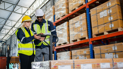 Warehouse workers team pulling a pallet truck and checking stock of goods before distribute to...