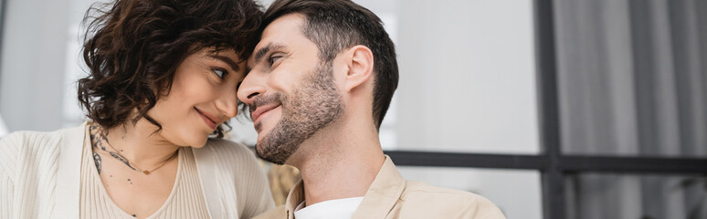 Tattooed woman looking at bearded husband at home, banner.