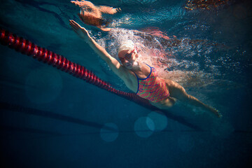 Front crawl. Young woman, professional swimmer in goggles and cap training, swimming in pool...