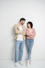 Brunette couple crossing arms while standing on white background.