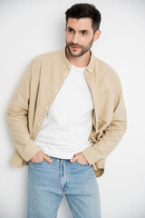 Bearded man in shirt and jeans posing on white background.