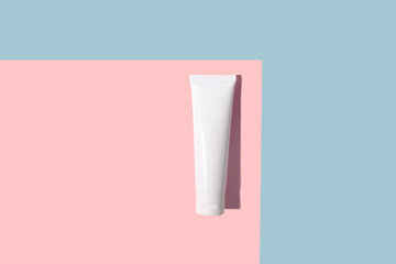 White cosmetic tube of cream with a hard shadow on a pink and blue background.