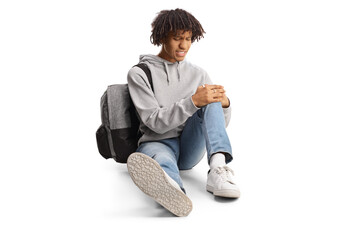 African american male student sitting on the floor and holding his injured knee