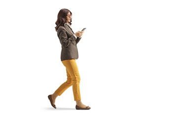 Full length profile shot of a young woman in formal clothing walking and using a smartphone
