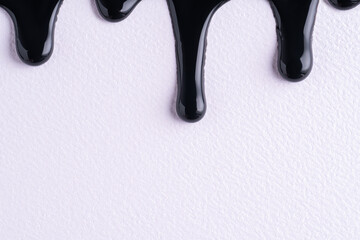 Black liquid drops of paint color flow down on white canvas. Abstract art. Black paint dripping on the white wall with copy space.