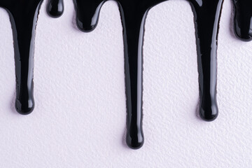 Black liquid drops of paint color flow down on white canvas. Abstract art. Black paint dripping on the white wall with copy space.