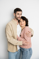 Fototapeta premium Adult couple hugging and looking away on white background.