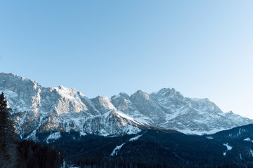 the beautiful eibsee in the foreground at the valley station of the zugspitzbahn in the south of germany where the mountains are illuminated by the sun and are covered with snow